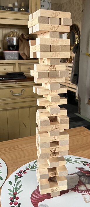 En stapel Jenga-klossar står balanserande på ett bord med en dekorativ bordstablett i bakgrunden.
