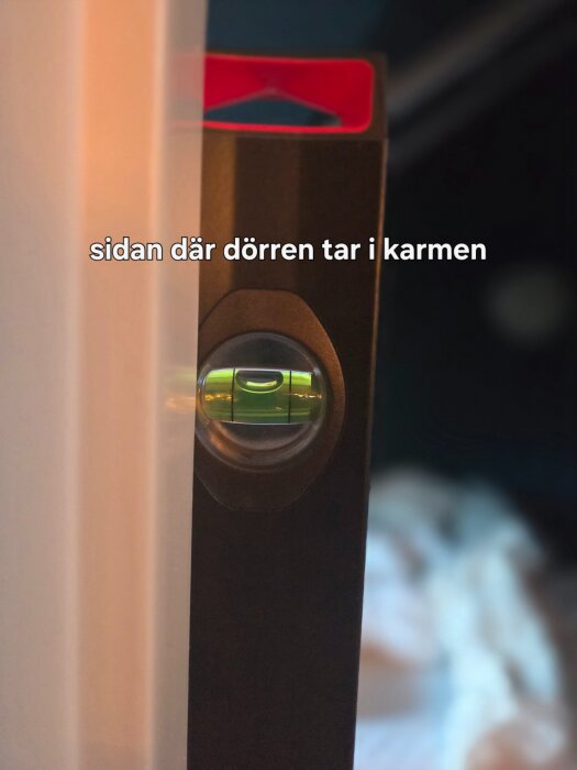 Vattenpass vid dörrkarm visar lutning; dörren tar i karmen.