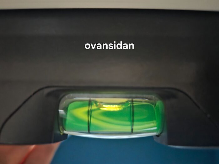 Vattenpass som visar lutning, där bubblan inte är i mitten, och texten "ovansidan" syns ovanför.