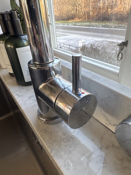 Köksblandare med droppande vatten och saknad insexssruv, placerad på en marmorerad bänkskiva framför ett fönster.