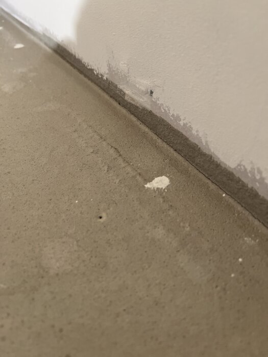 Flytspacklat golv med synlig upphöjning vid väggen och små rester av material.