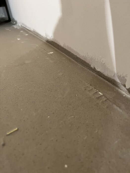 Osäkert golv med upphöjt glasfibernät vid väggen, rester av trämarkörer syns, flytspackel kan vara för tunt, förberedande för linoleumgolv.