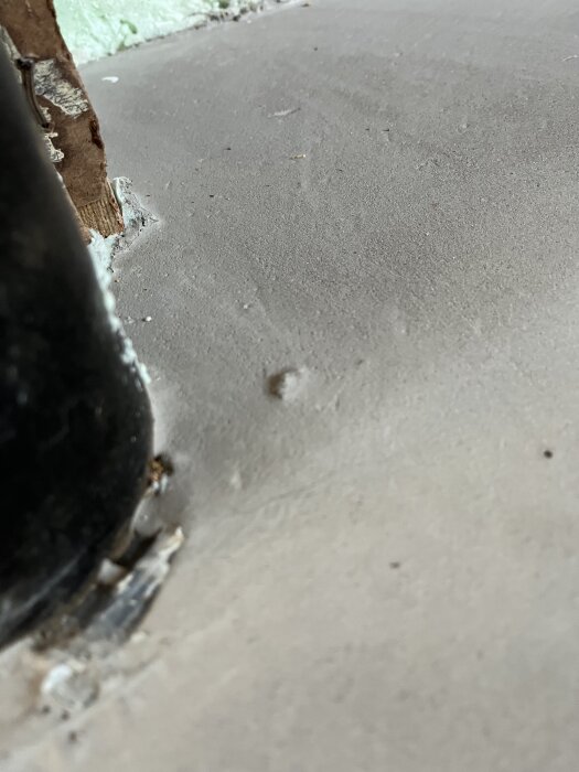 Ojämn yta av flytspacklat golv med uppbucklingar nära väggen och en svart pelare till vänster.