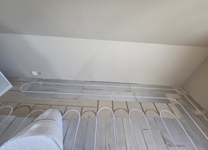 Golvvärmerör installerade i ett rum, med 20mm slang placerad mellan värmeplåtar på trägolv.