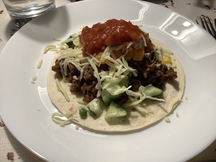 Tacos med köttfärs, tomatsås, ost, gurka och paprika på ett bord.