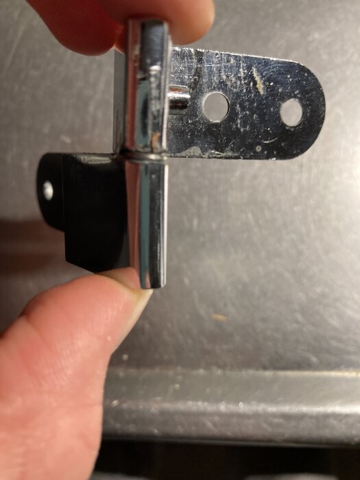 Gångjärn i metall med två hål, hålls i en persons hand; diskuteras om användning för skåpdörrar eller fönster.