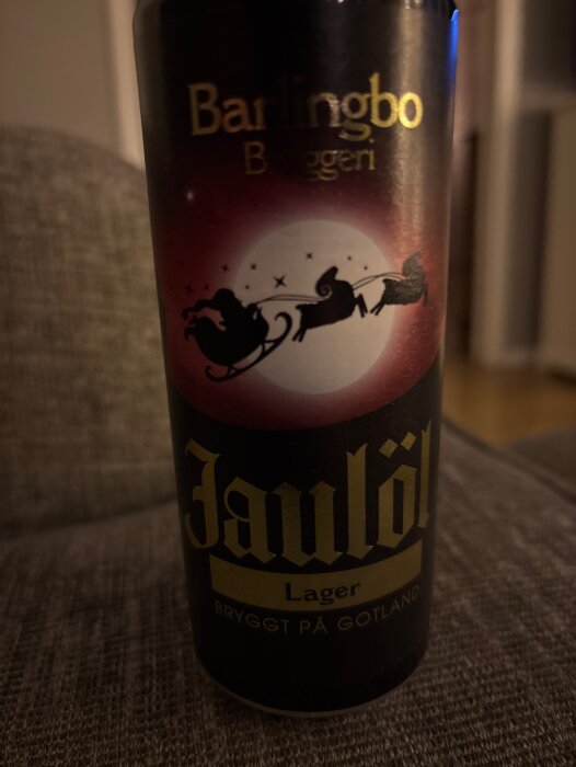 En burk julöl med en etikett av tomte i släde och renar mot en måne, från Barlingbo Bryggeri, står på en soffa. Bryggt på Gotland.
