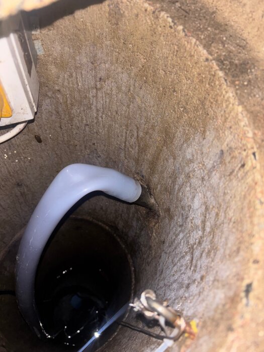 Insidan av en dagvattenbrunn med ett uppstickande rör och vatten vid botten.