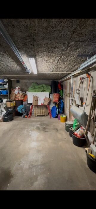 Ett garage med betonggolv, förrådsartiklar och ett tak klätt med träullit. Ajdå, lite rörigt!
