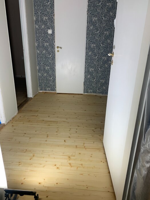 Nyslipat och hårdvaxoljat trägolv med vita dörrar och mönstrad blå tapet i renoverat rum.