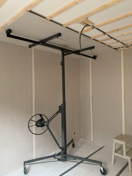 Gipshiss används för att montera skivor i tak vid renovering av rum. Skenor och träläkt synliga på taket, stege står bredvid.