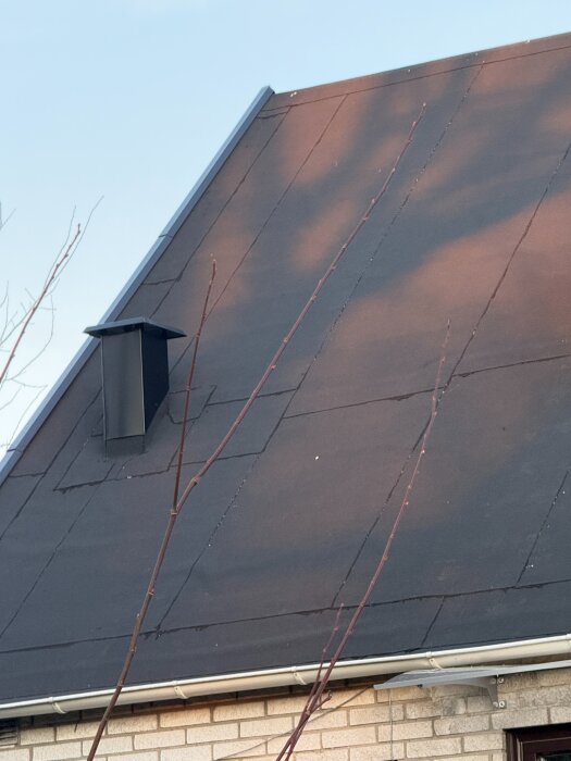 Tak med pappläggning, synlig skarvar och en svart avluftningshuv på ett nyrenoverat hus.