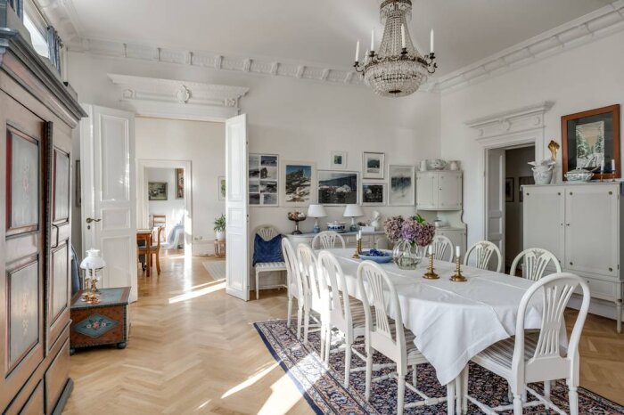 Elegant matsal i en av Karlstads finaste lägenheter, med ett stort bord, vita stolar, kristallkrona och konst på väggarna.