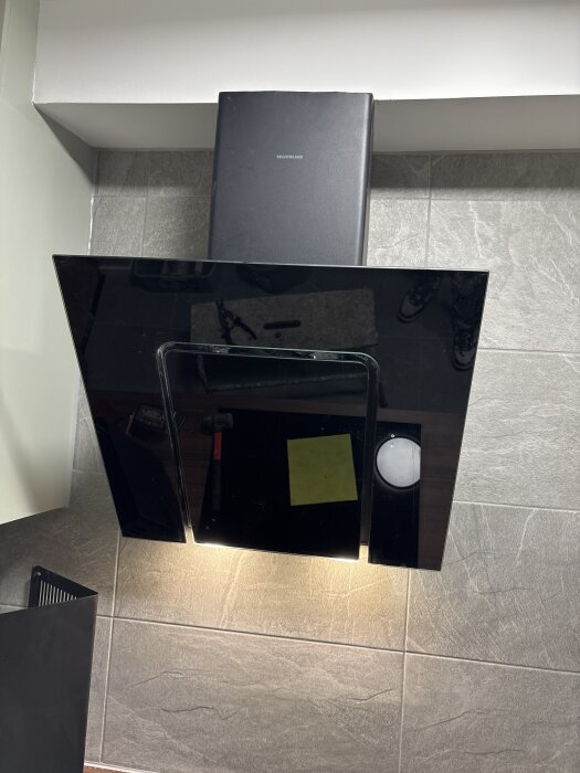 Svart köksfläkt av märket Silverline installerad mot en vägg med grå kakelplattor; fläkten är igång och lyser upp arbetsytan under.