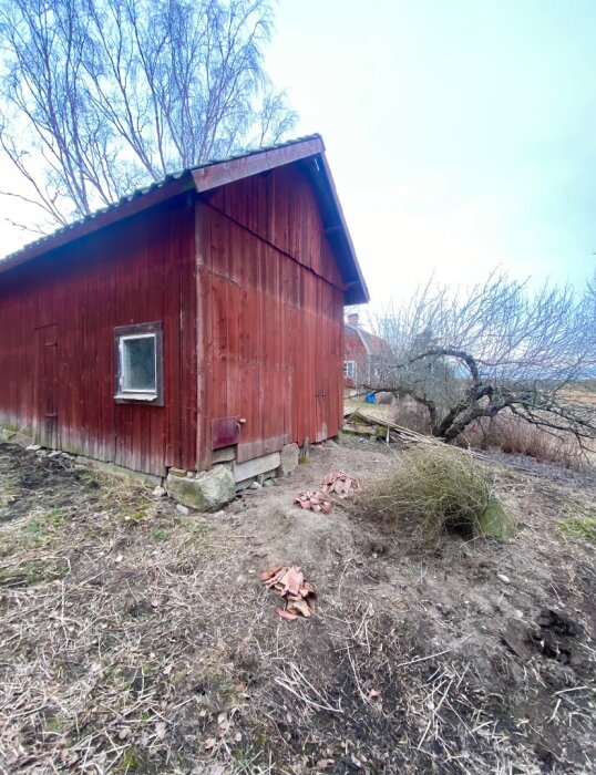 Rött hönshus med torpargrund och syllstockar på hörnstenar. Rutten syll synlig, omgiven av grus och vissna växter.