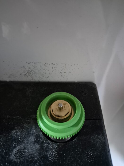 Grön justeringsskruv på svart underlag, del av verktyg utan manual.