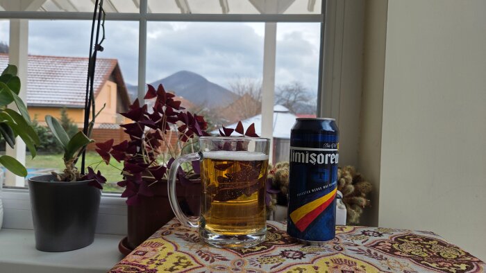 Ölglas och burk på bord vid fönster med utsikt över tak och berg, omgivna av krukväxter.