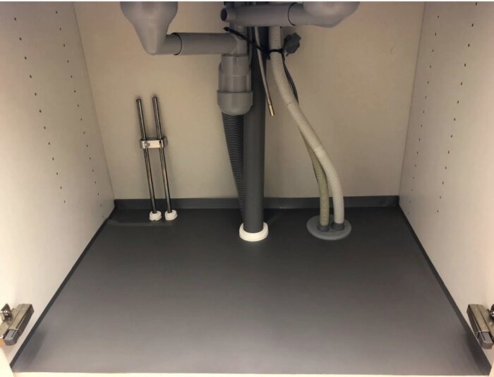 Vattenrör och avloppsrör under ett diskbänksskåp, komplett med genomföringar vattensäkert installerade i botten av skåpet.