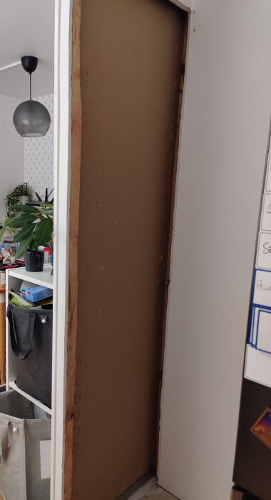 Öppen vägg utan hylla, med synliga träreglar och gips, i ett rum med hylla och växter i bakgrunden.