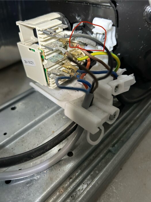 Närbild på kylskåpskompressor med färgade kablar och markerat stift vid en vit plastdel och metallkontakt.