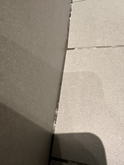 Kakelgolv möter kakelvägg i dusch med synliga fogar och kalkavlagringar. Vatten samlas längs vinkeln, vilket kan påverka fogen.
