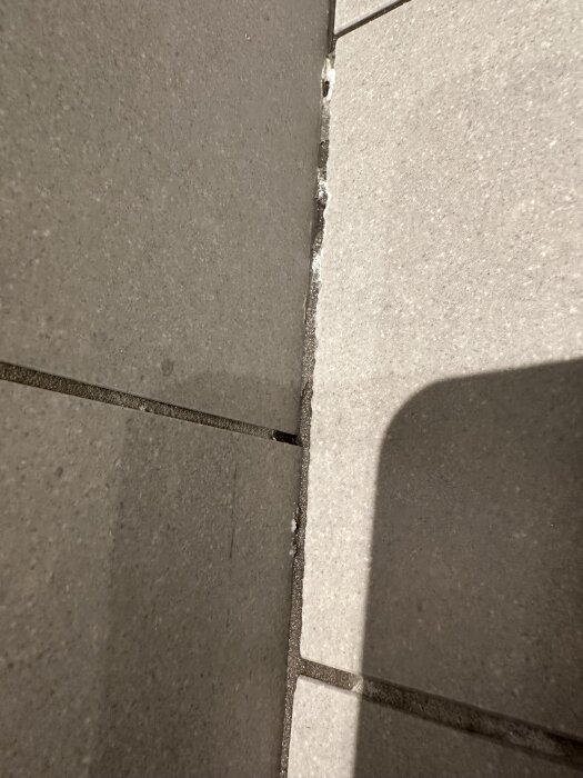 Sliten fog med kalkavlagringar mellan kakelplattor i duschhörn, där vatten samlas vid golv- och väggvinkel.