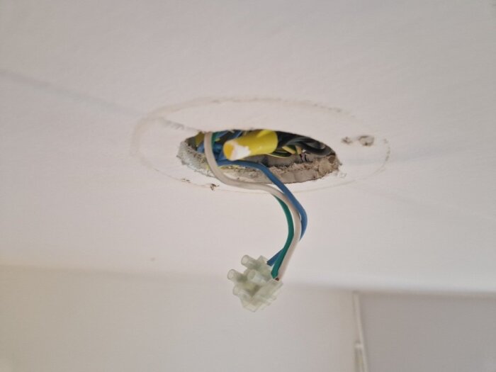 Kablar hänger från ett tak, redo för installation av lamputtag. Gamla kabelfärger synliga, osäkerhet kring korrekt inkoppling.