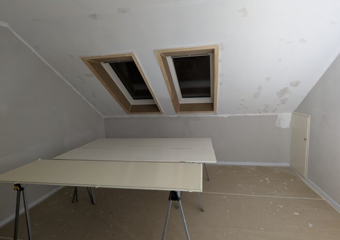 Orenoverat kontor med två takfönster och vita bord på bockar redo för slipning och målning. Väggar är förberedda för tapetsering.