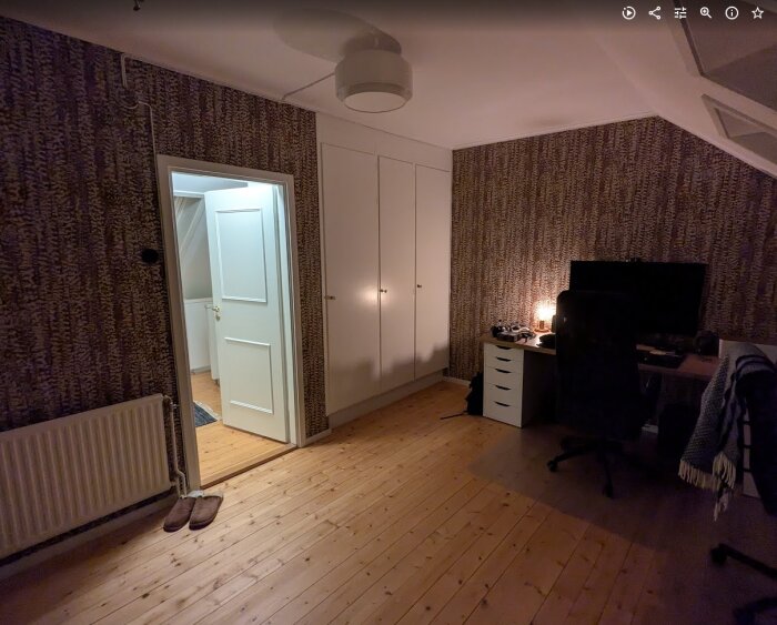 Renoverat kontor med tapetserade väggar, ljusa trädörrar, skrivbord med datorskärm, och taklampa i ett mysigt inrett rum.