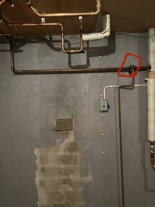 Rörinstallation i en källare med en kopparledning och ventil, ventilen markerad med röd cirkel.