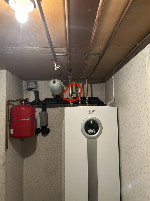IVT bergvärmepump är installerad i källaren, omgiven av kopparrör och ett rött expansionskärl. En ventil är markerad med en röd cirkel.