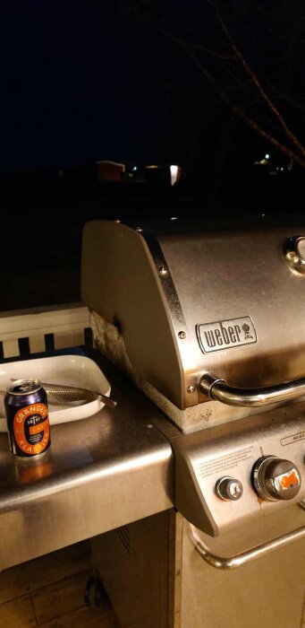 Gasolgrill av märket Weber på en altan i skymningen, med en burk Gränges Lager och en bakform på grillens avlastningsyta.