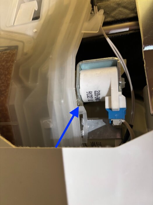 Vit plastkomponent med blå pilar pekande mot den, vilket indikerar en potentiell läckagekälla i en apparat.