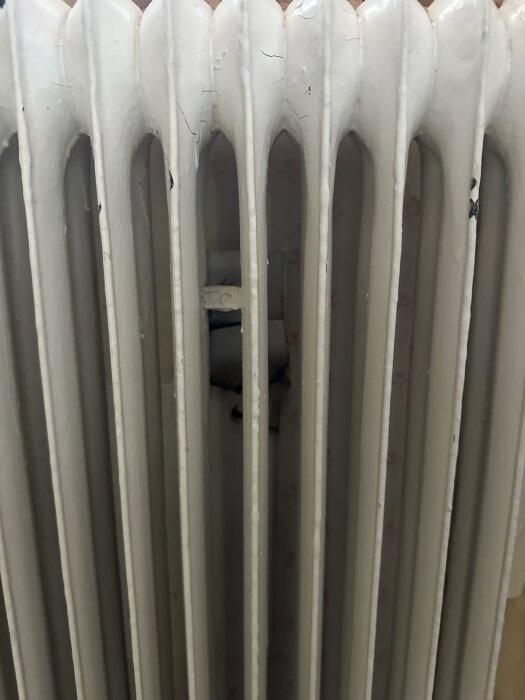 Närbild på en vit sektionsradiator med sprickor i färgen, visar fästet och området bakom radiatorn där gipsvägg ska monteras.