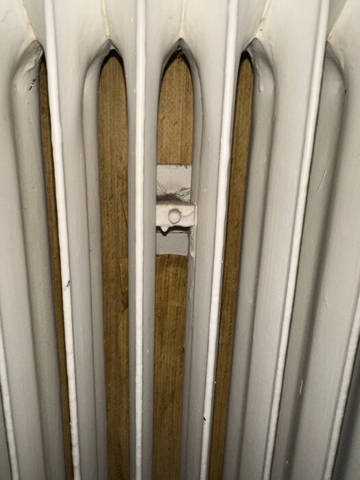 Radiator fastsatt på väggen med bultar och muttrar, träpanel bakom.