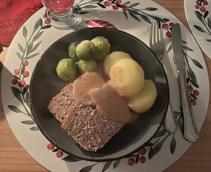 Köttfärslimpa serverad med kokt potatis, brysselkål och pepparsås på en tallrik med dekorativa kanter.