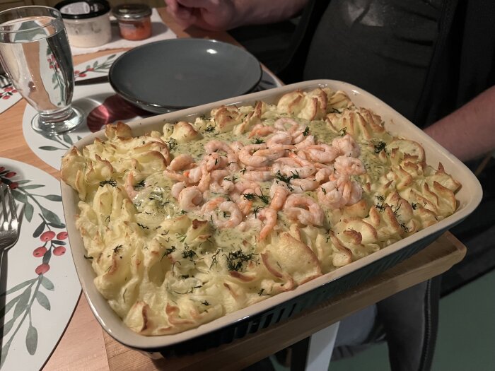 Fiskgratäng med lax, torsk, räkor, hemgjort mos, citron- och dillsås i en ugnsform på ett dukat bord.