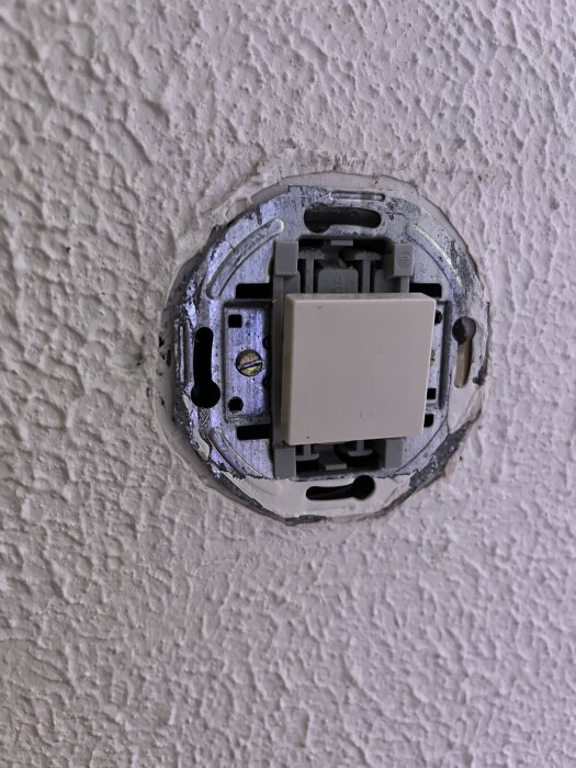 Inbyggd väggströmbrytare i en grov yta av betongvägg, saknar yttre ram och visar det elektriska inre.