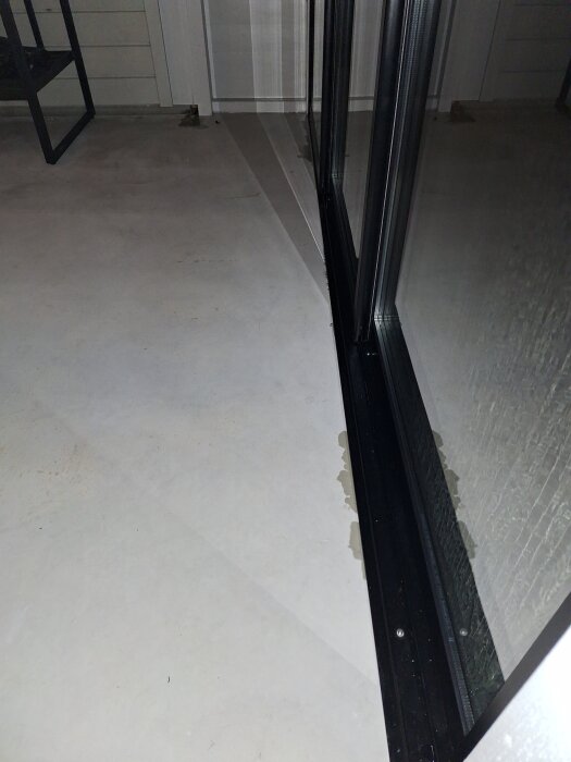 Betonggolv i inglasat uterum med ojämnheter längs skenan som orsakar vattenläckage vid regn.