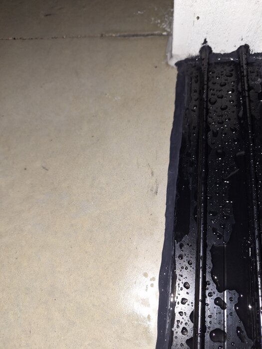 Betongplatta och svart skena i uterum med vattenstänk, ojämn betong orsakar läckage vid regn.