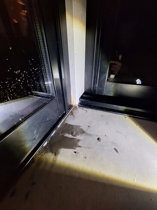 Vattenläckage vid skarv mellan glasparti och betonggolv i uterum under slagregn, med synlig ojämnhet på golvytan.