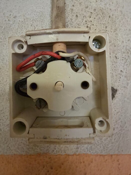Elektrisk kopplingsdosa med synliga röda och svarta ledningar för belysningsinstallation, betongvägg i bakgrunden.