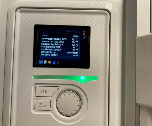 Display på värmesystem visar temperaturer och inställningar. Kontrollpanel med OK-knapp, vred och skärm med information om värme och driftstatus.