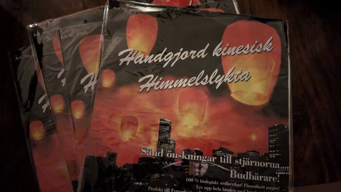 Förpackning med handgjorda kinesiska himmelslyktor, mot en bakgrund av en stadssilhuett och en himmel fylld med schiffonliknande lyktor i skymningen.