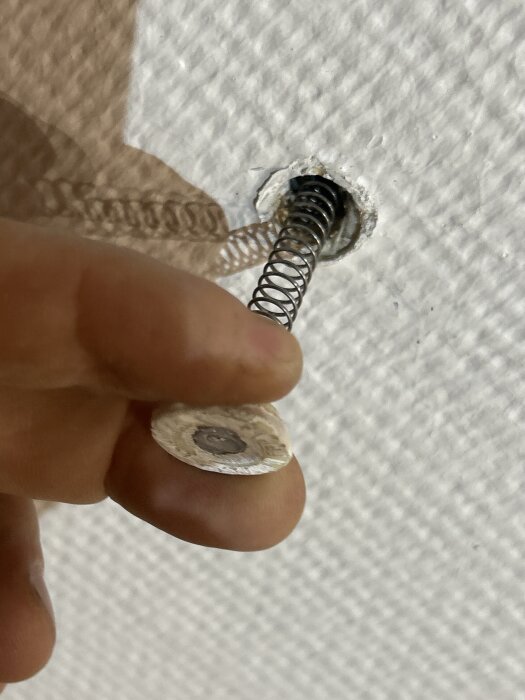 En hand håller en fjädrande vit plugg delvis insatt i ett hål i taket.