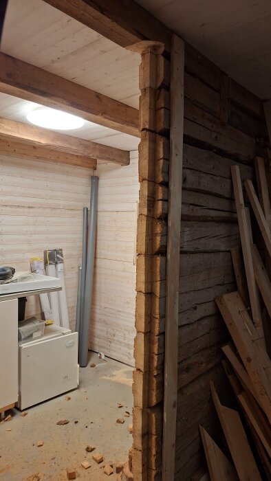 Renoverad trävägg med träbitar på golvet, verktyg och byggmaterial bredvid.