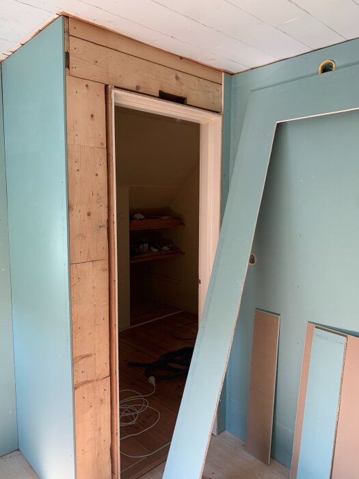 Renovering av kontor och gästrum med OSB och gipsskivor vid dörröppning. Exponerat trä och kablar synliga, takpaneler på plats.