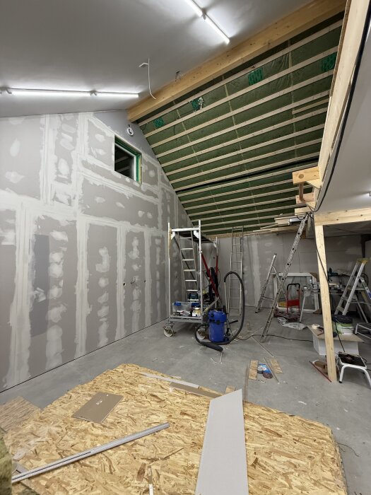 Garage under renovering med öppet tak och oisolerade väggar, flera stegar och verktyg synliga på golvet, förberett för installation av billyft.