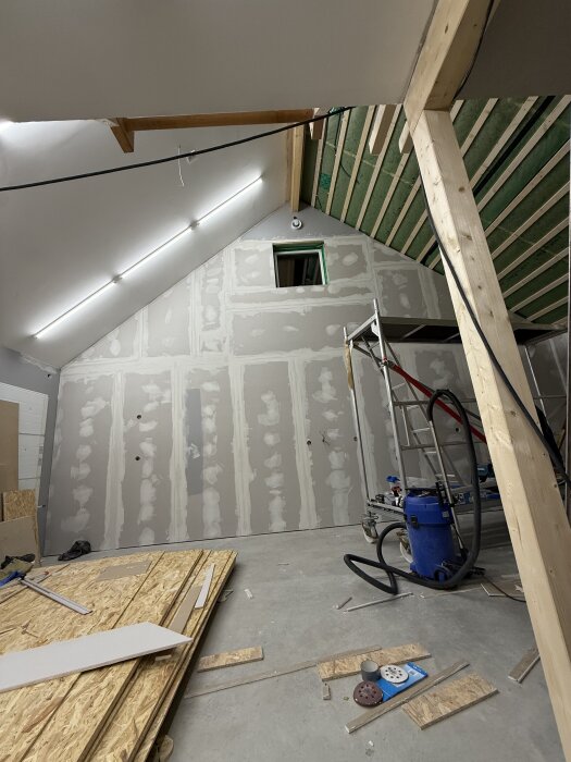 Garage under renovering med insida av tak och väggar, stege, byggmaterial och verktyg synliga på golvet.