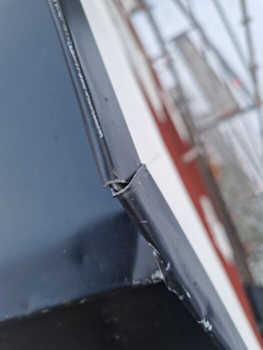 Skadat hörn på ett nylagt mansardtak med repor och anmärkningar på plåtarbetet, visar detaljer vid kanten av taket.